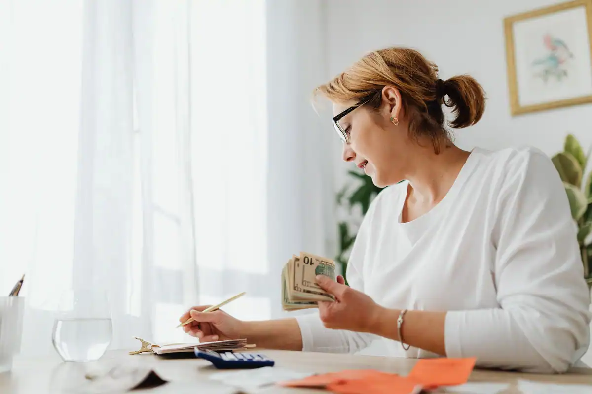 Antreprenoare care își calculează finanțele cu bani, calculator și caiet
