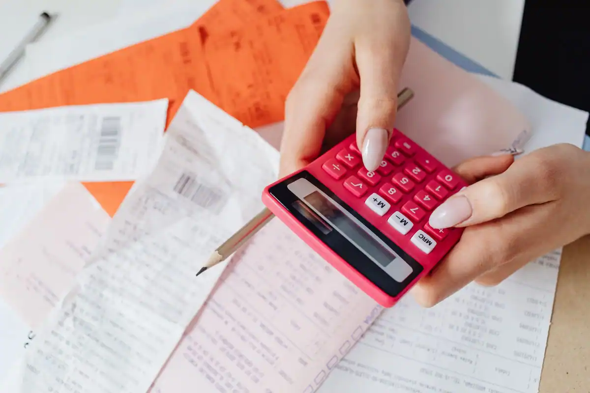 Mâini care folosesc un calculator roz printre chitanțe și documente