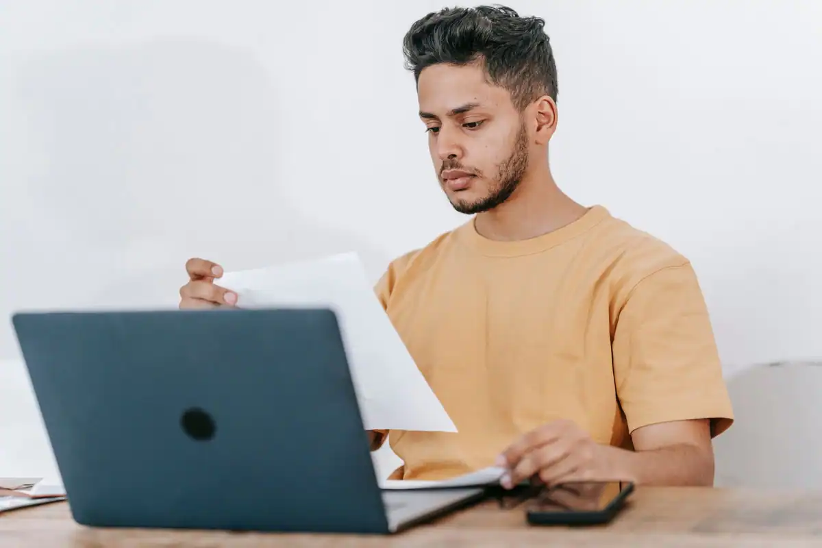 Tânăr care citește notițe lângă laptop în timp ce studiază online