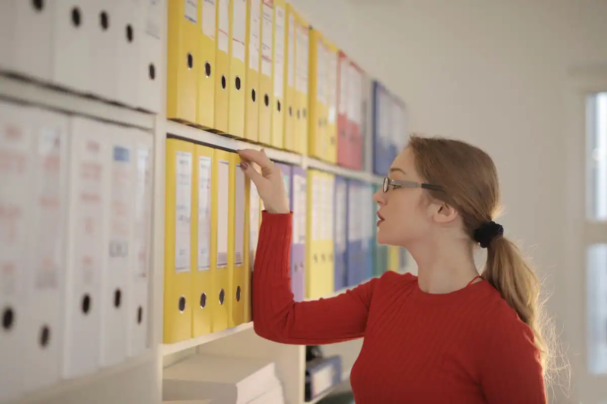 Angajată care caută documente în bibliorafturi colorate
