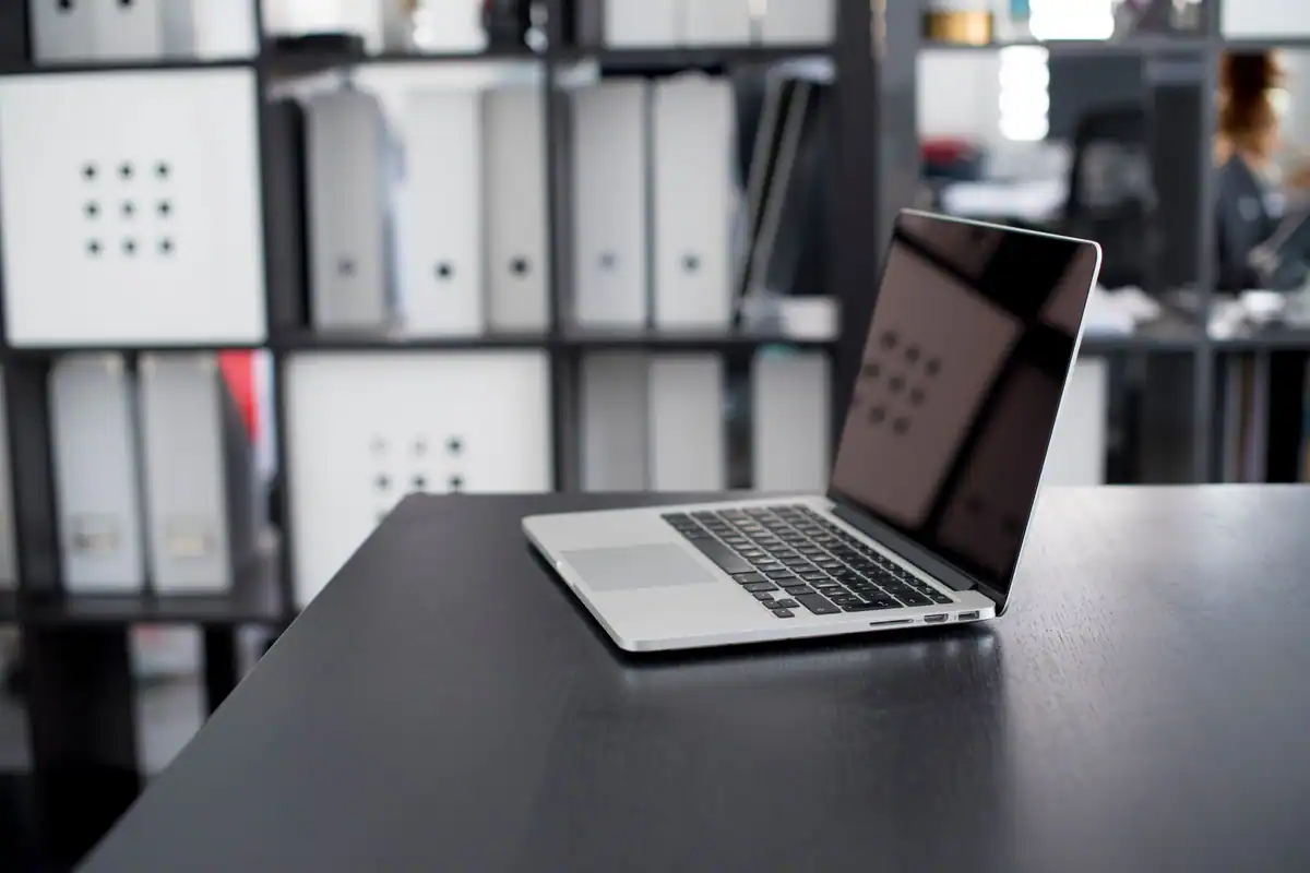 Laptop pe un birou minimalist, cu rafturi în fundal