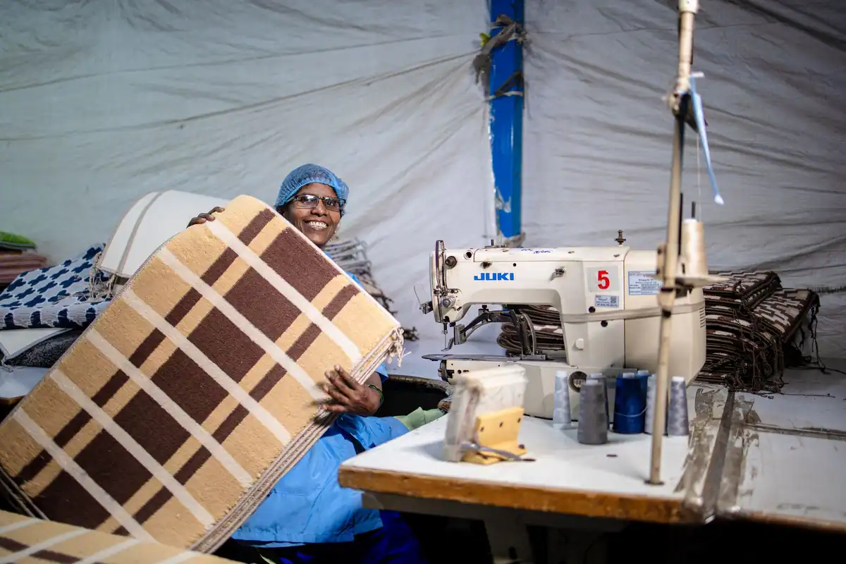 Lucrătoare zâmbitoare cu un produs textil lângă o mașină de cusut industrială