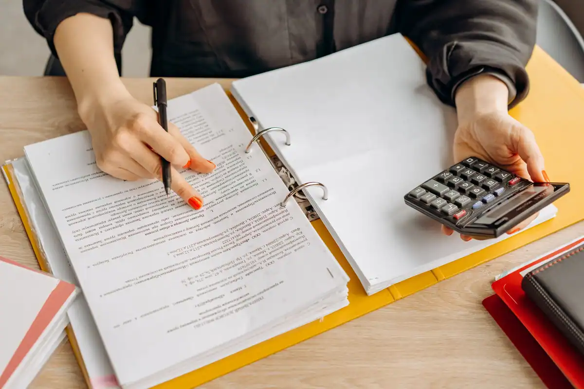 Femeie care verifică documente cu un calculator pe o masă din lemn