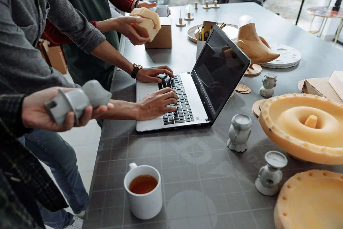 Mâini pe laptop într-un atelier creativ cu prototipuri și modele 3D