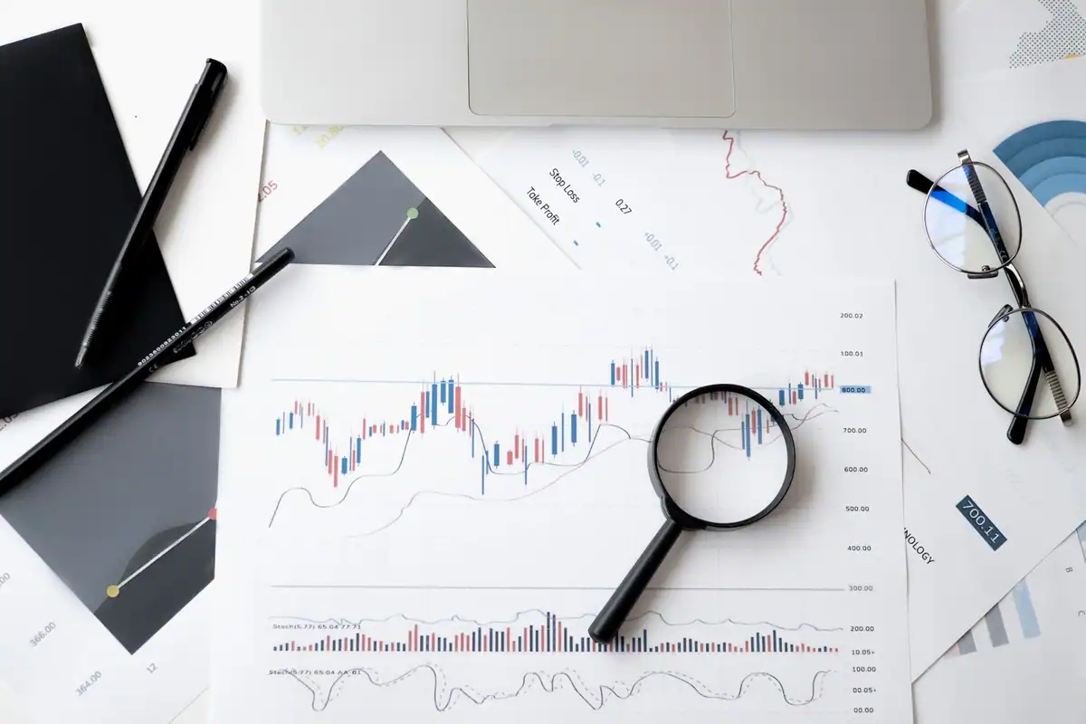 Documente de analiză financiară cu lupă, pixuri și ochelari
