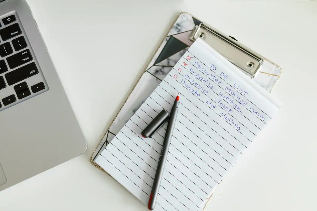 Listă de sarcini pe clipboard lângă un laptop și un pix