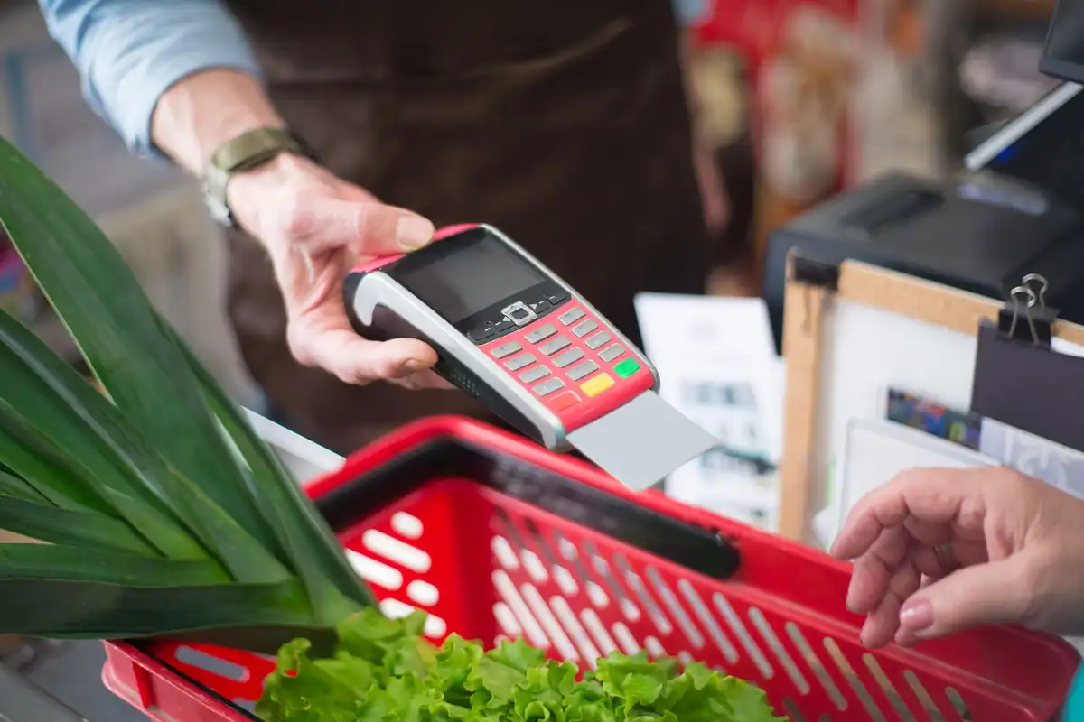 Plată contactless la casa unui magazin, cu legume proaspete în coș