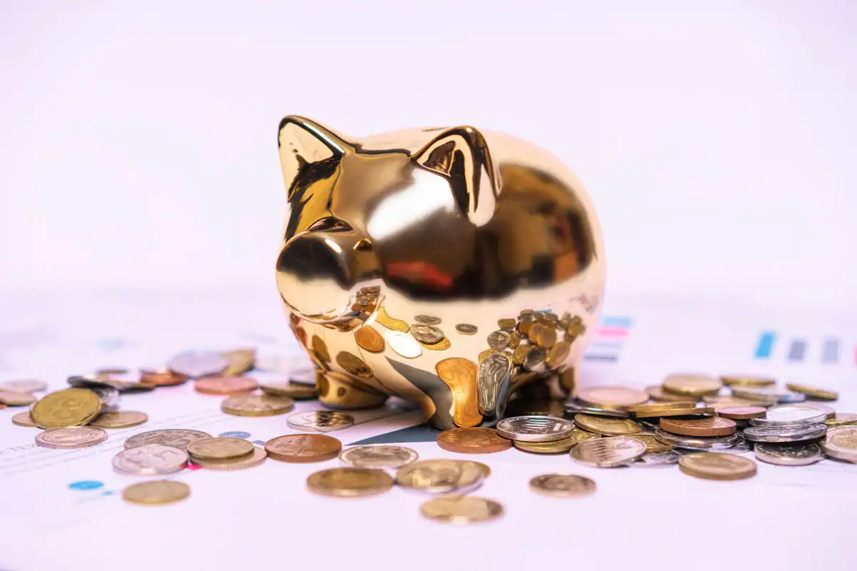 Pușculiță aurie pe documente financiare, cu monede împrăștiate