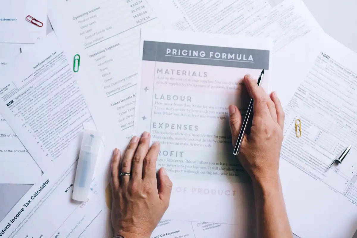 Mâini care organizează documente și calcule de preț pe birou