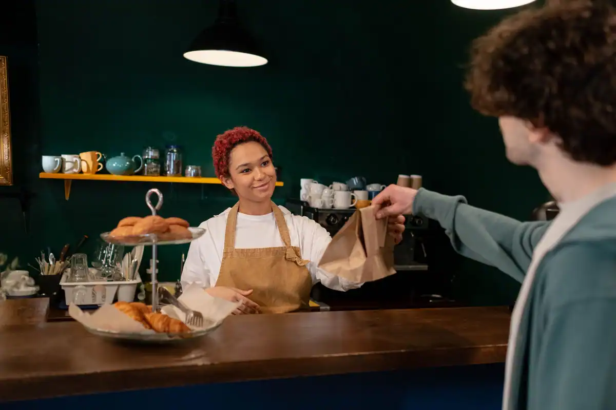 Barista care îi întinde unui client produse de patiserie la tejghea