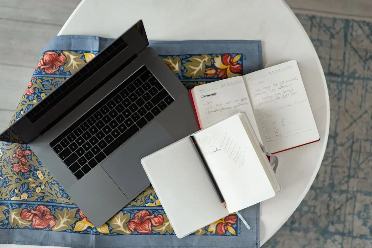 Laptop, caiete și creion văzute de sus pe o față de masă cu model
